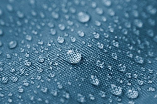 droplets of water bead up on a piece of blue fabric, showing the effect of stain repellant or waterproofing chemical treatments